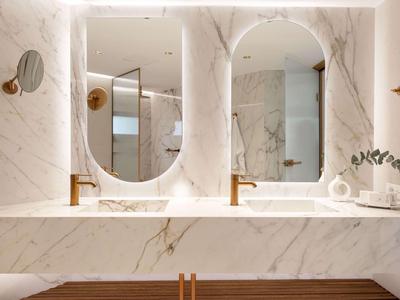 Luxuriöses Badezimmer mit Marmorwänden, zwei ovalen Spiegeln und Waschbecken mit goldenen Armaturen.