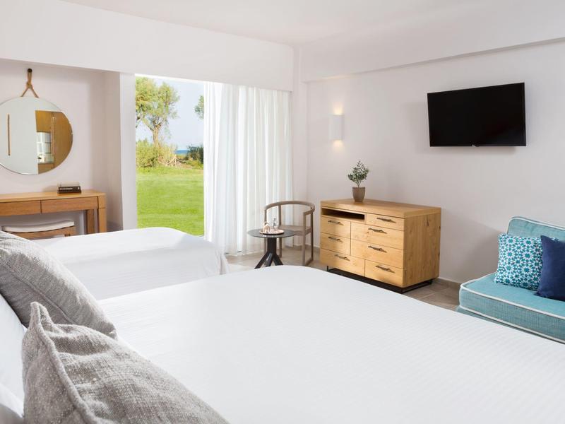 Moderne hotelkamer met twee bedden, bank, dressoir en uitzicht op een groene wei.