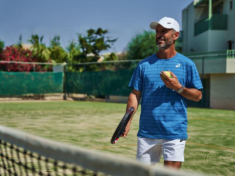 Een man in sportkleding speelt tennis op een buitenbaan bij zonnig weer.