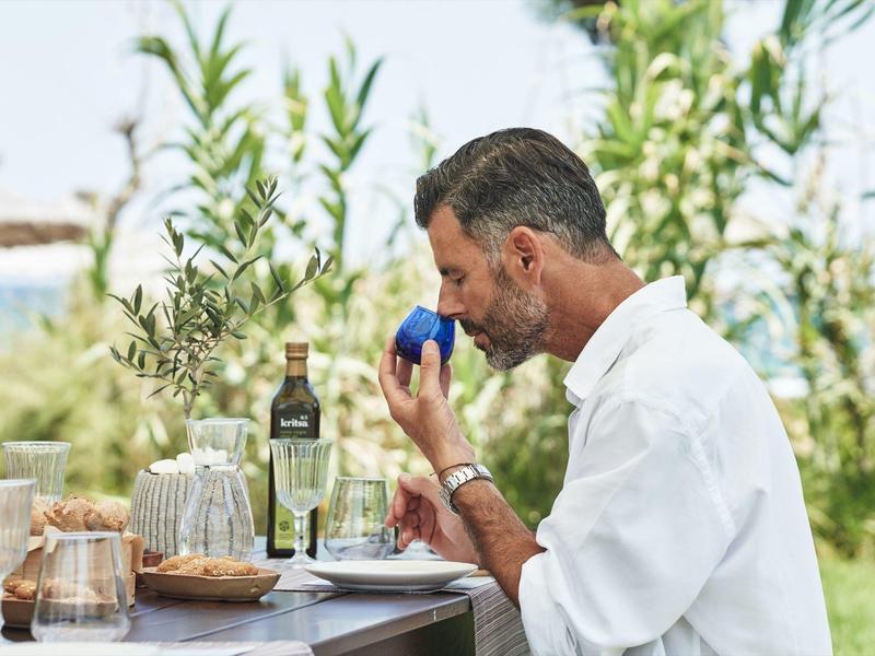 Een man geniet van eten en wijn aan een buitentafel met groene begroeiing op de achtergrond.