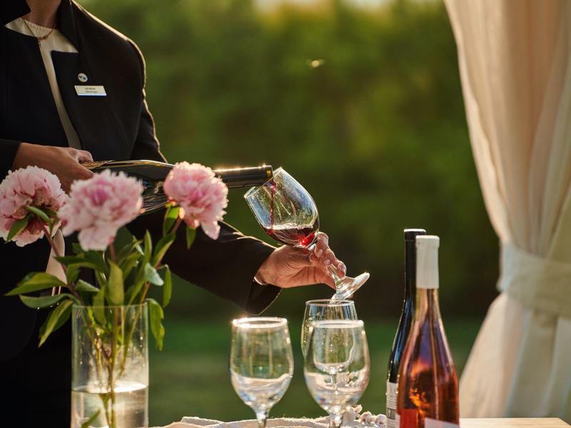 Iemand schenkt wijn in een glas naast bloemen op een gedekte tafel.