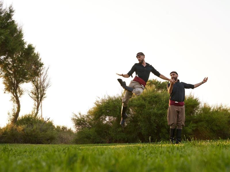 Twee mannen in traditionele kleding poseren op een groen weiland met bomen.