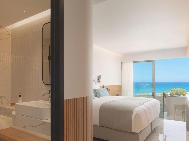 Modern hotelkamer met tweepersoonsbed en zeezicht via grote ramen.