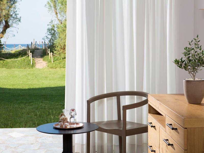 Moderne houten stoel naast houten tafel en gordijn met uitzicht op groene tuin en zee.