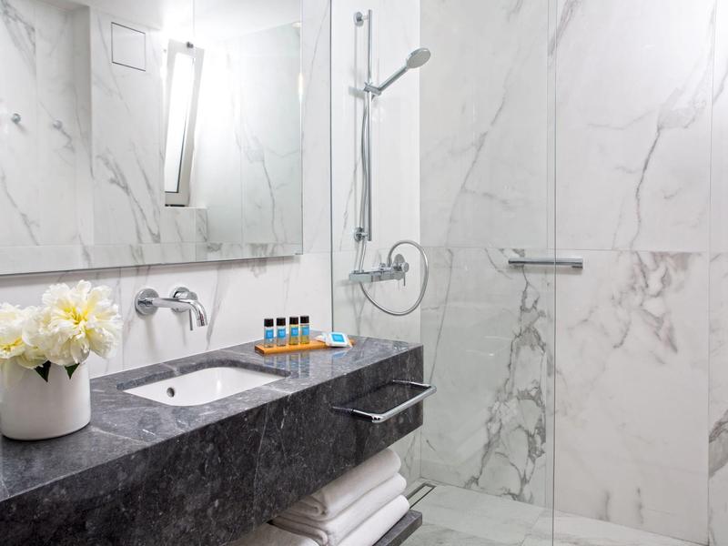 Moderne badkamer met marmeren muren, zwart stenen aanrecht en douchegedeelte met glazen wand.