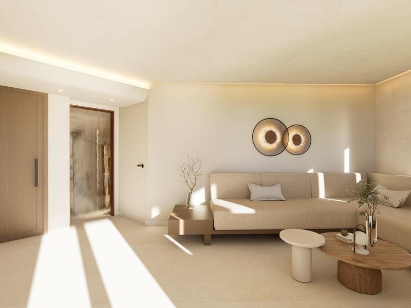 Lichte, moderne woonkamer met beige tinten, bank, koffietafels en open toegang tot de badkamer.