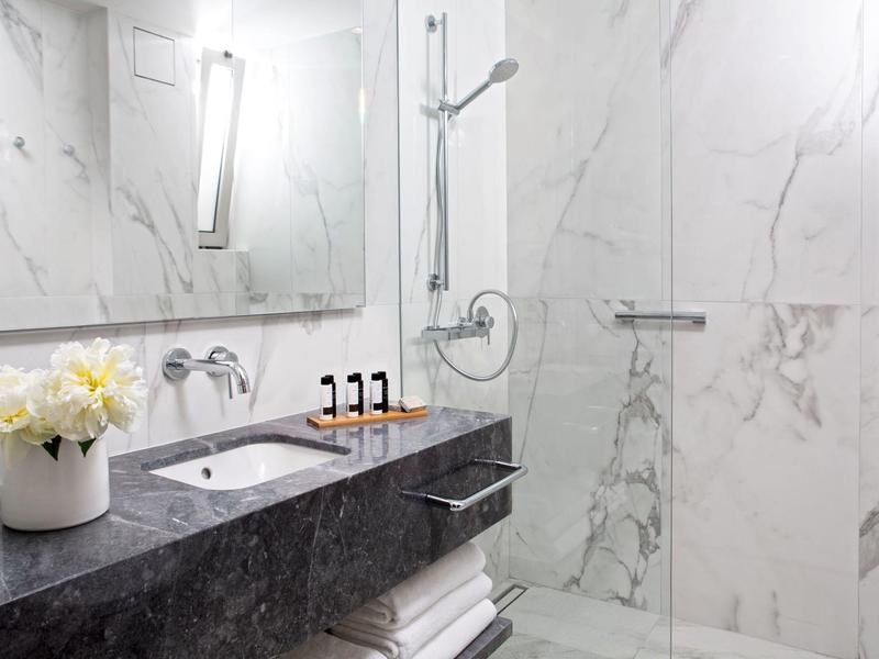 Moderne badkamer met marmeren muren, donkergrijs aanrechtblad en bloemenarrangement.