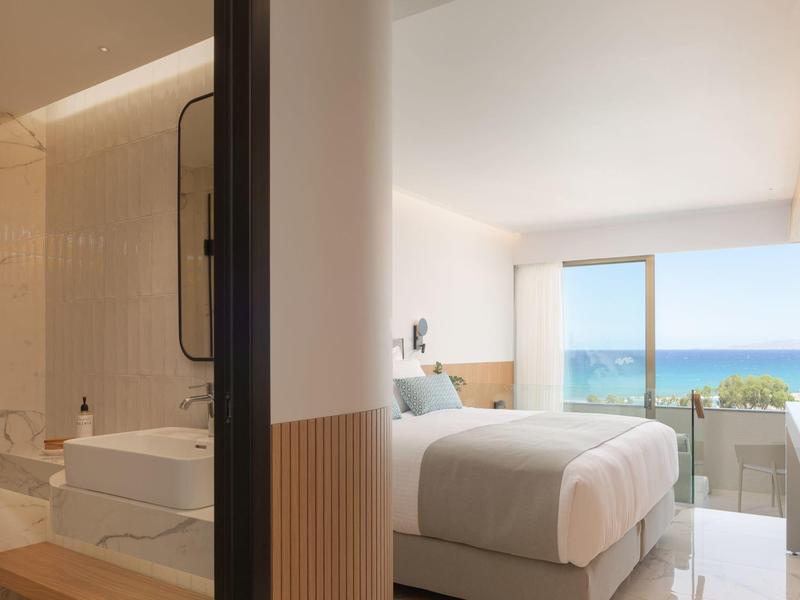 Licht hotelkamer met zeezicht, tweepersoonsbed en moderne badkamer.