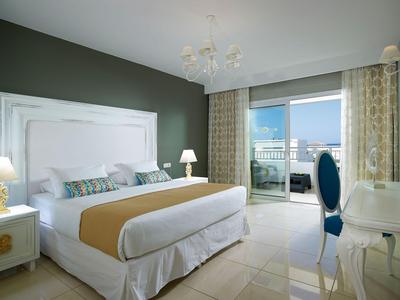 Chambre d'hôtel lumineuse avec grand lit, mur vert et balcon avec vue sur la ville.