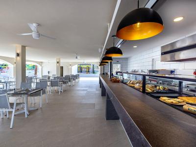 Modern openlucht eetgedeelte met tafels en een bakkerijbalie onder zwarte hanglampen.