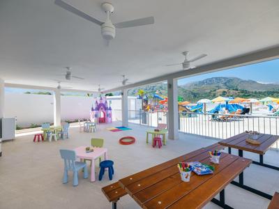 Open ruimte met zitplaatsen en speelgoed met uitzicht op zwembad en bergen.