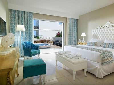 Lichte hotelkamer met wit bed, blauwe stoelen en open terraszicht.