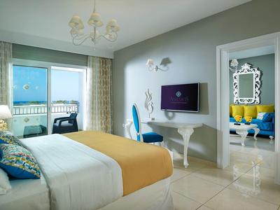 Lichte hotelkamer met groot bed, gele deken en uitzicht op balkon bij zee.