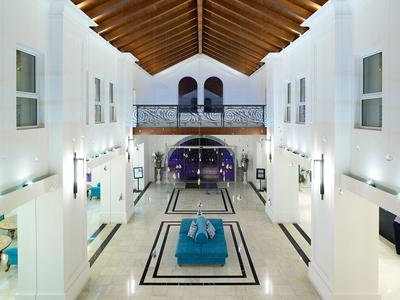 Licht hotelontvangst met hoog houten plafond, witte muren en blauwe zitruimte.