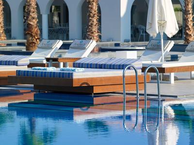 Vue d'une piscine avec chaises longues et parasols à côté de palmiers dans un hôtel.