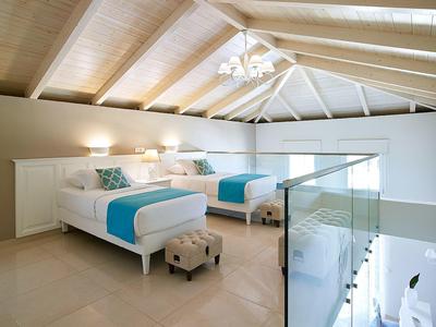 Ruime zolderkamer met twee bedden, witte houten plafonds, glazen balustrade en turquoise accenten.