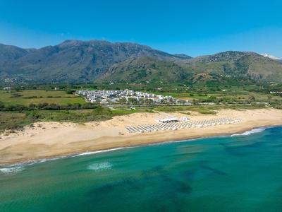 Weißer Sandstrand mit Sonnenschirmen, grüne Hügel im Hintergrund und blauer Himmel.