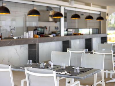 Terrasse de restaurant moderne avec chaises blanches et tables sous des suspensions noires.