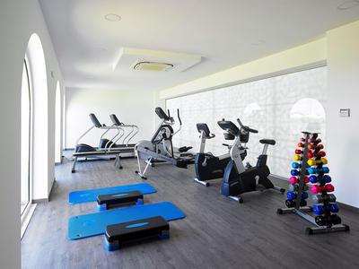 Salle de sport lumineuse avec tapis roulants, vélos, steps et haltères colorés dans un hôtel.