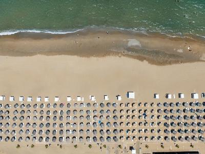 Luchtfoto van een strand met nette rijen parasols en ligstoelen langs de kustlijn.