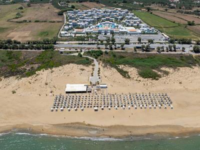 Luchtfoto van een strand met parasols, ligstoelen en een groot gebouw in de buurt.