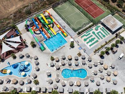 Luchtfoto van een waterpark met zwembaden, kleurrijke glijbanen, parasols en tennisbanen.