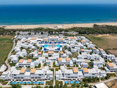 Luchtfoto van een groot strandresort met zwembaden, witte gebouwen en de zee op de achtergrond.