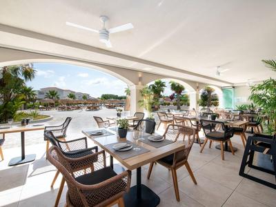 Buitenterras met tafels en rotan stoelen met uitzicht op een zwembad en tuin.