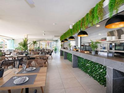 Restaurant moderne avec décor en bois et plantes, espace lumineux et cuisine ouverte.