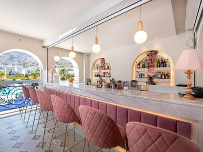 Bar d'hôtel moderne avec sièges roses, bar éclairé et vue sur la terrasse et l'eau.