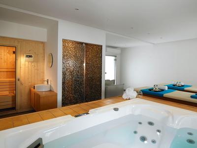 Moderne wellnessruimte met bubbelbad, sauna en ligbedden in lichte kamer.