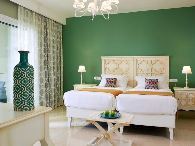 Modern hotelkamer met twee eenpersoonsbedden, groene accentmuur en stijlvolle decoratie.