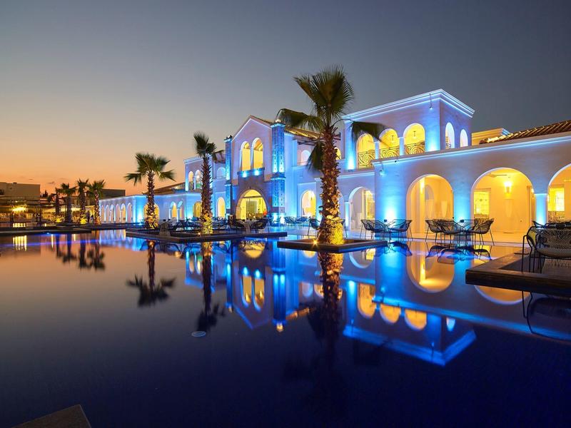 Elegant resortgebouw verlicht bij schemer met palmbomen en zwembadreflecties.