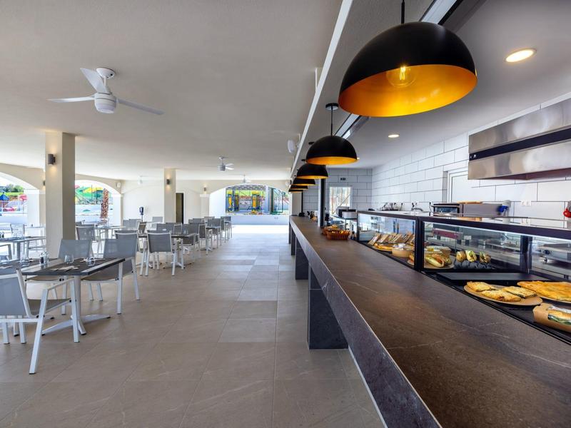 Modern openlucht eetgedeelte met tafels en een bakkerijbalie onder zwarte hanglampen.