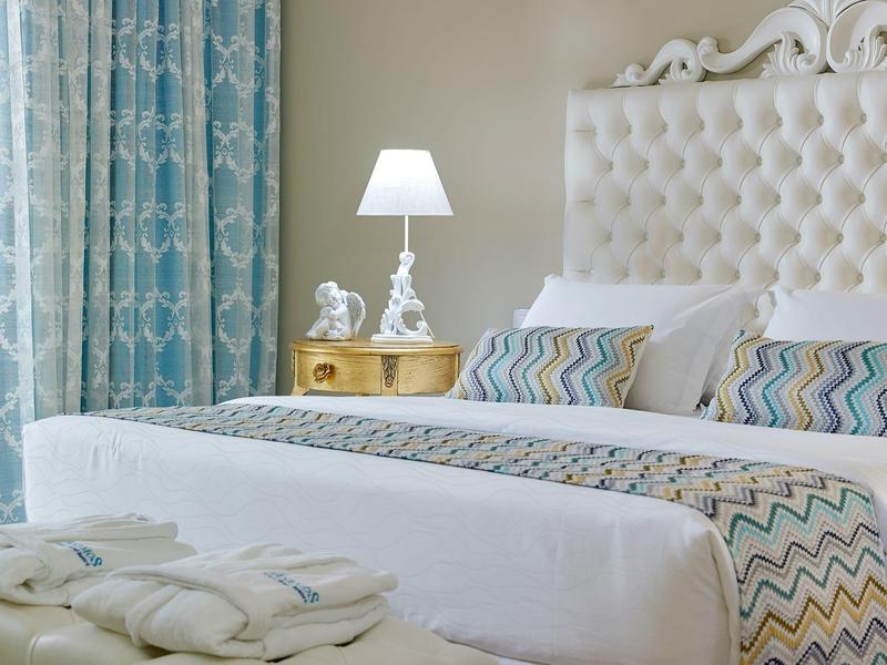 Elegant hotelbed met wit linnengoed, patroon kussens, nachtkastje en lamp