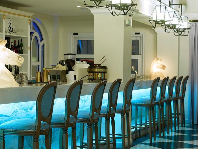 Elegante bar met hoge stoelen en blauw verlichte bar onder moderne hanglampen.