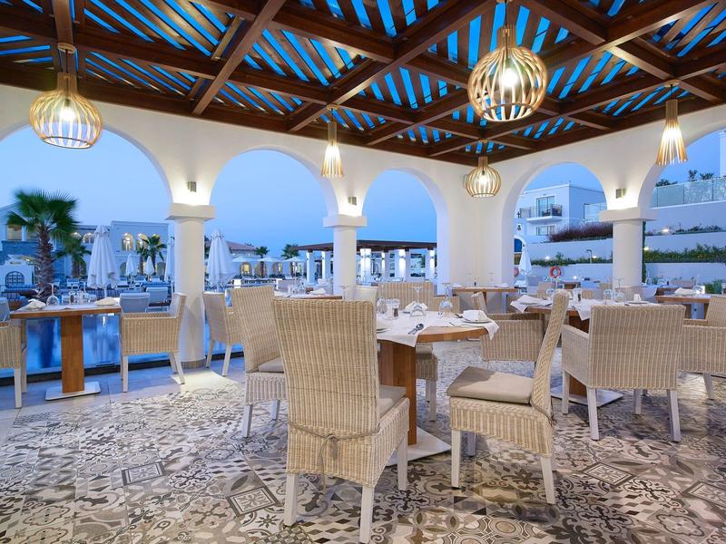 Buitenrestaurant van hotel onder houten dak met rieten stoelen en tafels bij het zwembad.