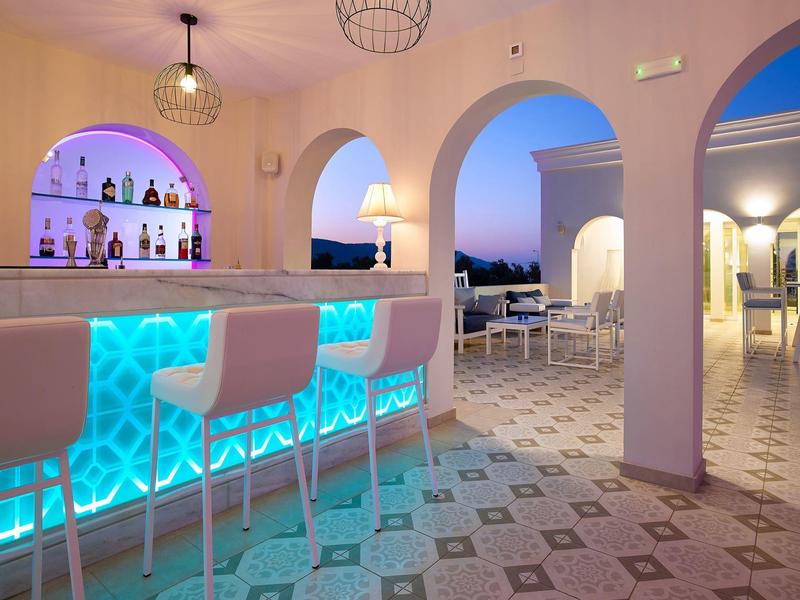 Modern hotelbar met blauw verlichte toonbank, krukken, bogen en buitenzitplaatsen bij schemer.