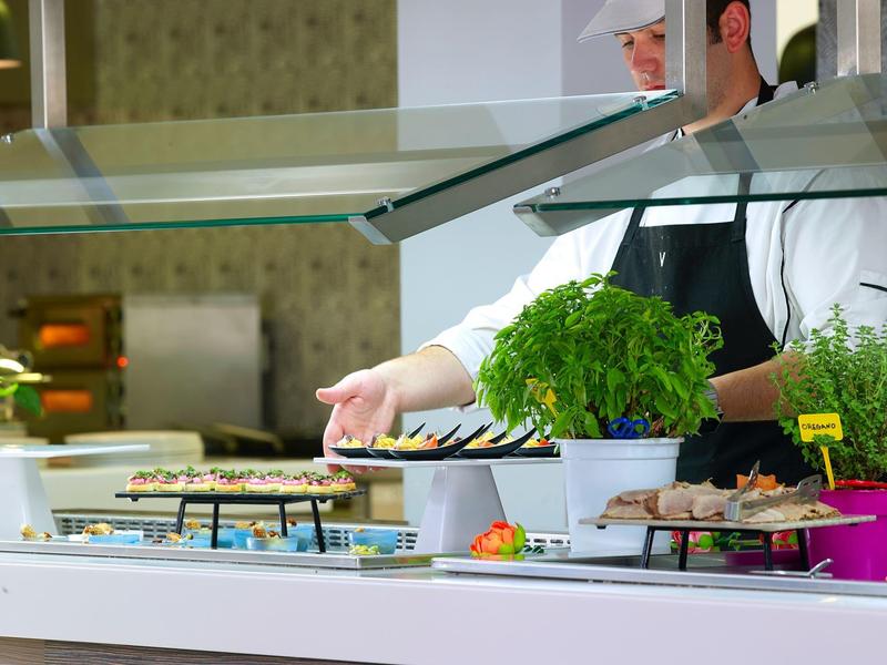 Chef achter toonbank die eten bereidt met verse kruiden en hapjes tentoongesteld.