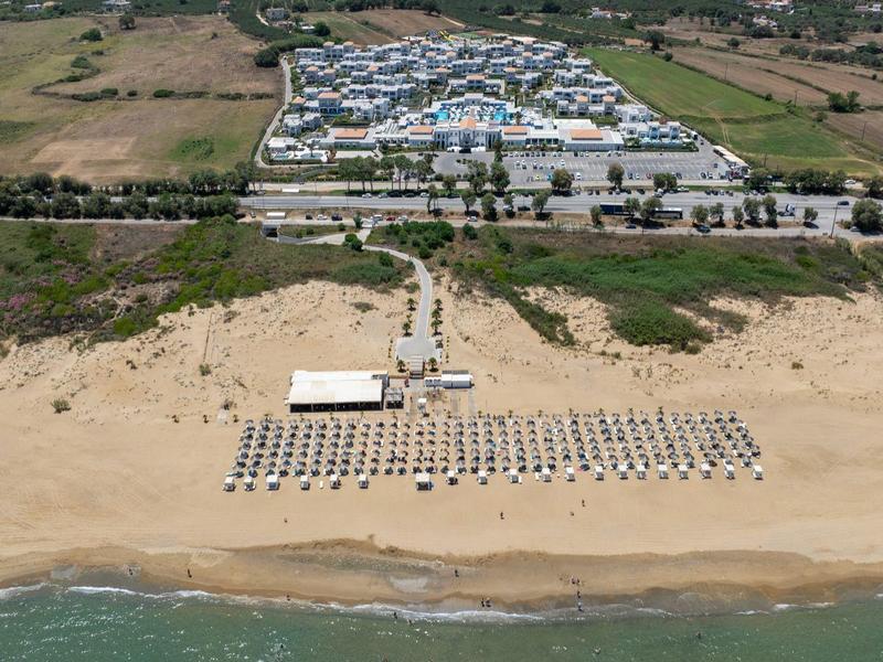 Luchtfoto van een strand met parasols, ligstoelen en een groot gebouw in de buurt.
