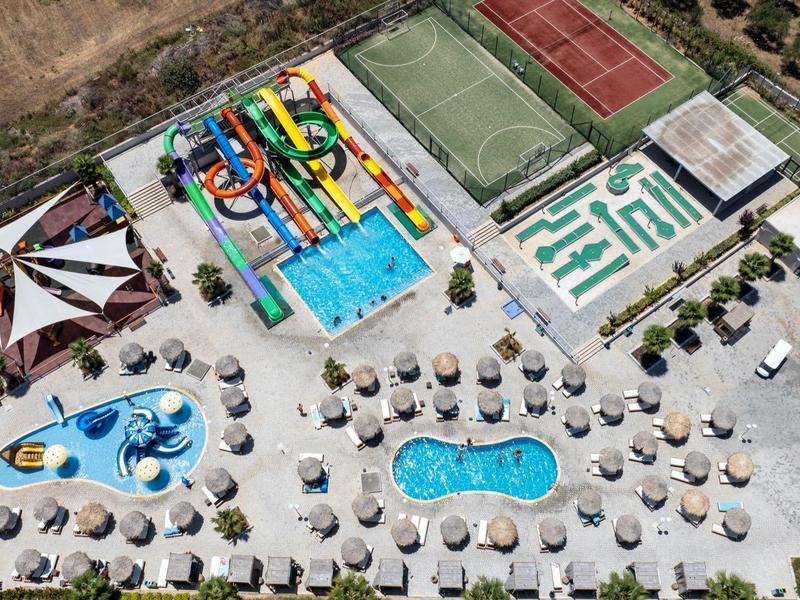 Luchtfoto van een waterpark met zwembaden, kleurrijke glijbanen, parasols en tennisbanen.