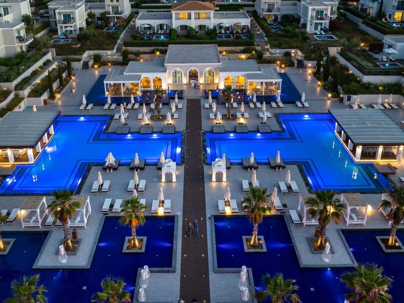 Luxe hotel met groot blauw verlicht zwembad en symmetrische zitgedeeltes buiten in de avond.