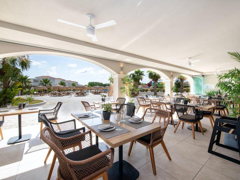 Buitenterras met tafels en rotan stoelen met uitzicht op een zwembad en tuin.