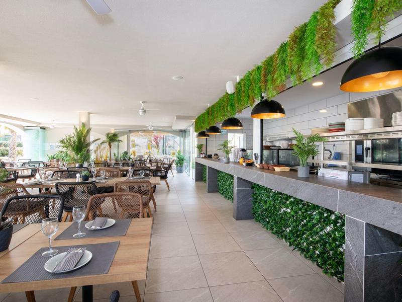 Moderne restaurantinterieur met hangplanten, houten tafels en zwarte hanglampen.
