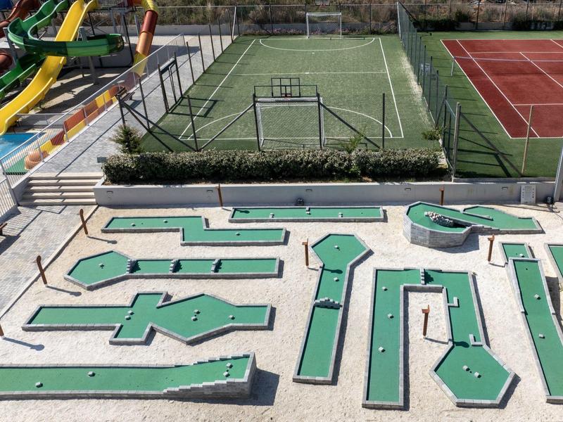 Buitenspeelplaats met minigolfbaan naast tennisbanen en glijbanen in een recreatiegebied.