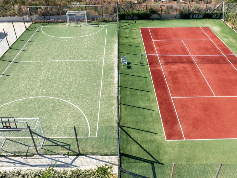 Buiten sportterrein met een groen voetbalveld en een rood tennisbaan naast elkaar.