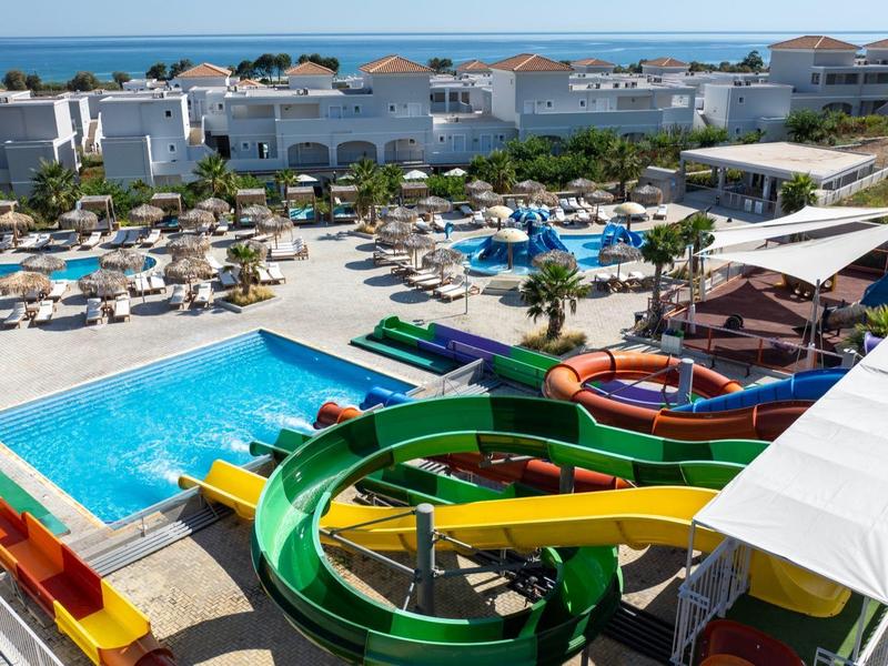 Groot hotelzwembad met kleurrijke glijbanen, ligstoelen en parasols onder felle zon.