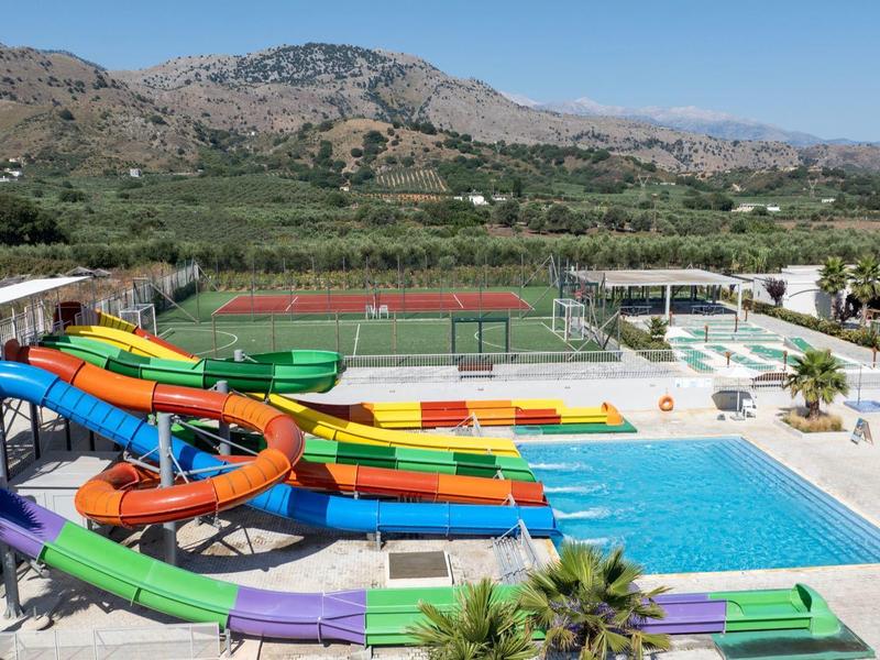 Groot buitenwaterpark met kleurrijke glijbanen en zwembaden omringd door bergen en groen.