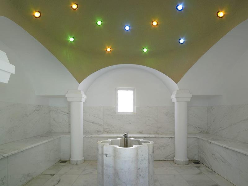 Interieur van een historische hammam met marmeren muren en gekleurde lichten aan het plafond.
