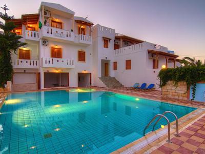 Hôtel blanc moderne avec piscine illuminée et chaises longues au coucher du soleil.